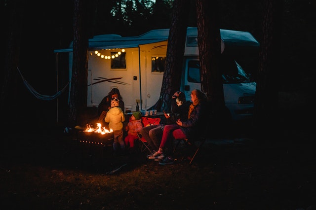 Family on holiday next to a caravan with a campfire